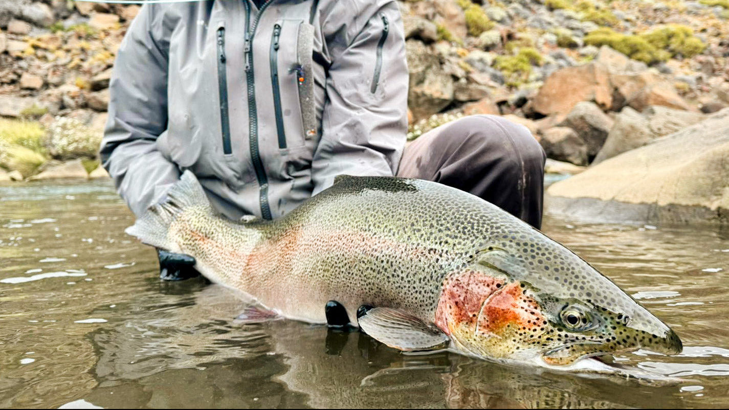 Man holding a large fish caught while fishing in a rocky stream.